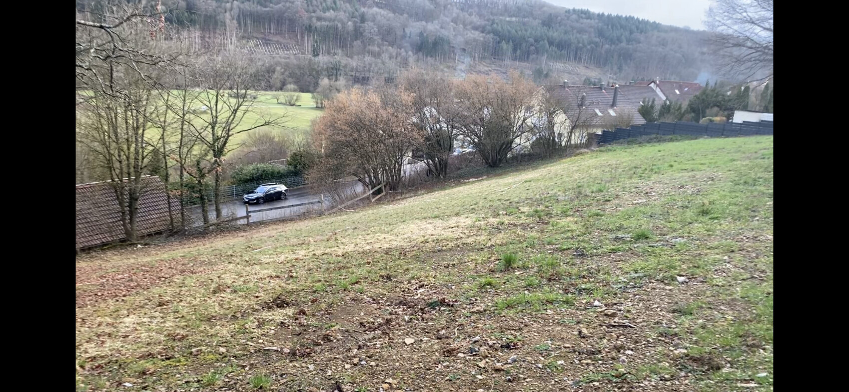 Schwarzer SUV fährt eine kurvige Straße, flankiert von Bäumen und Häusern im Hintergrund.