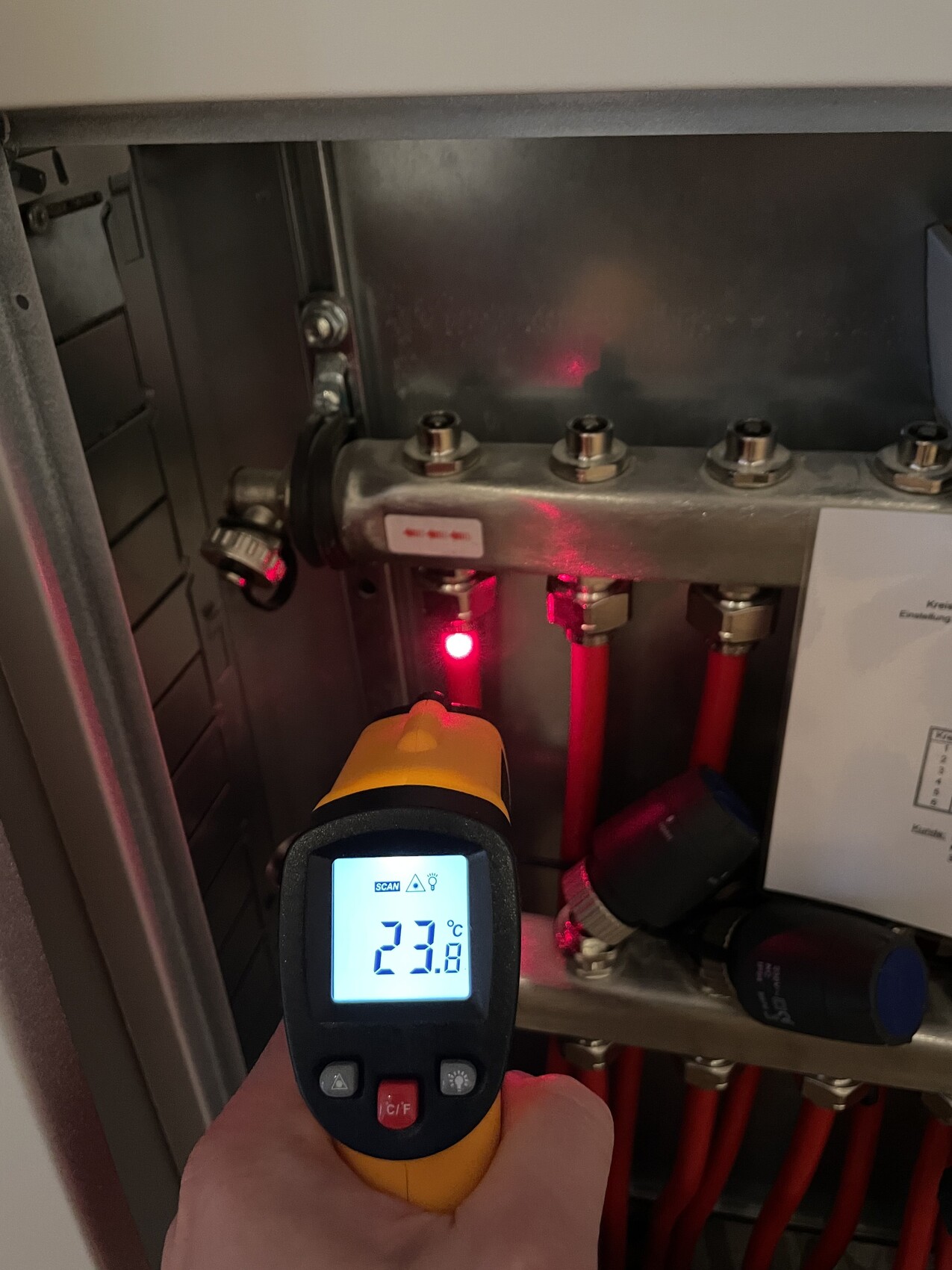 Handliches Infrarot-Thermometer misst Temperatur im Schaltschrank; Anzeige 23,8 °C, rote LED.