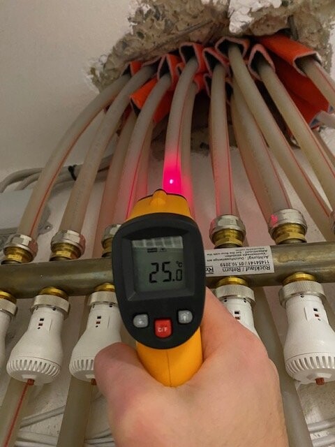Hand mit IR-Thermometer misst Rohrleitungstemperatur; roter Laser, Anzeige 25°C