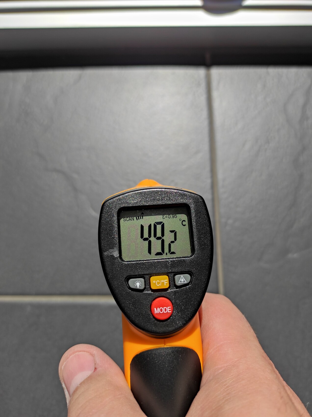 Nahaufnahme eines Infrarot-Thermometers zeigt 49,2 °C auf Metalloberfläche