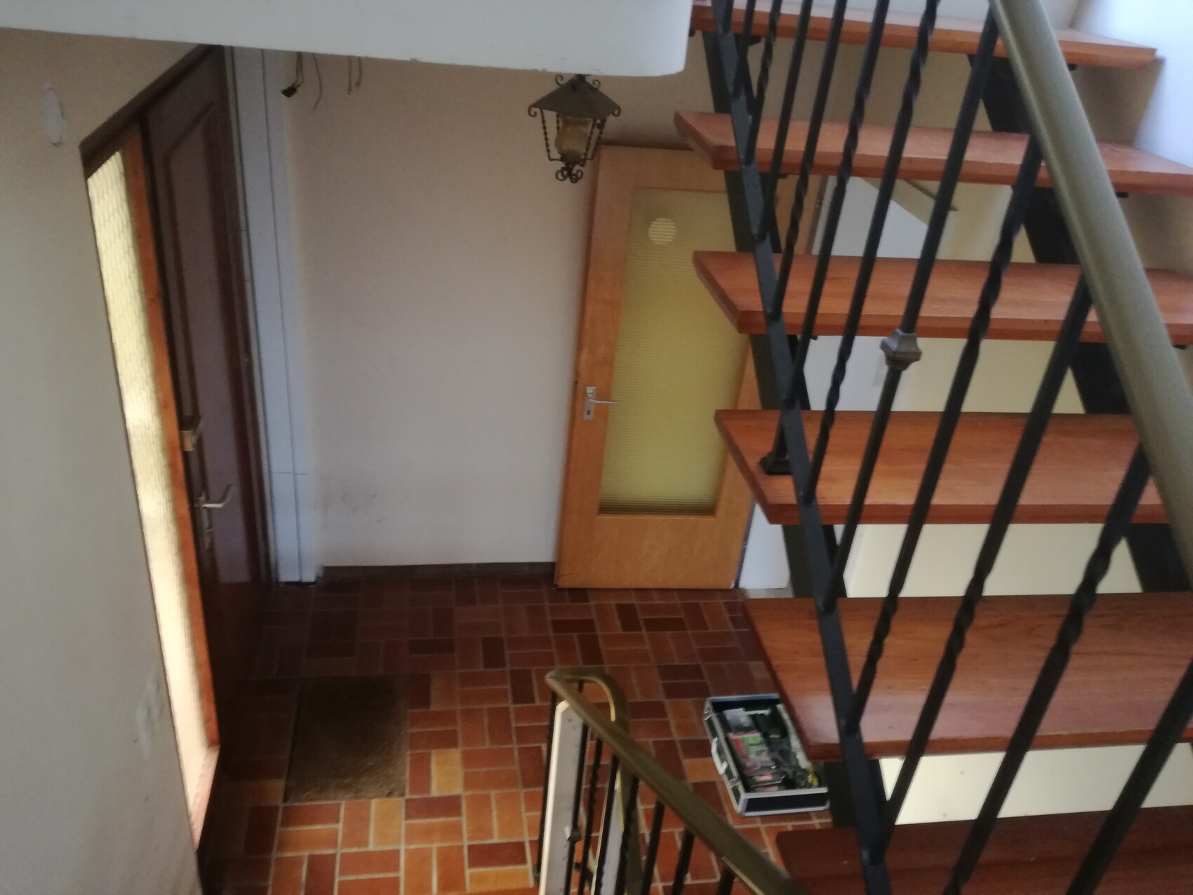 Innenansicht eines Treppenhauses mit Holzstufen, schwarzem Geländer und Tür unten.