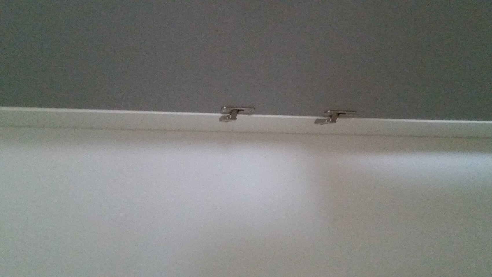 Nahaufnahme einer weißen Türkante mit zwei Metall-Scharnierelementen, daneben eine graue Wand.