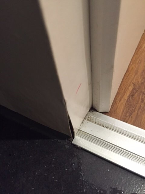 Nahaufnahme einer Innentür-Schwelle mit Metallleiste, weißer Wand und Holzboden.