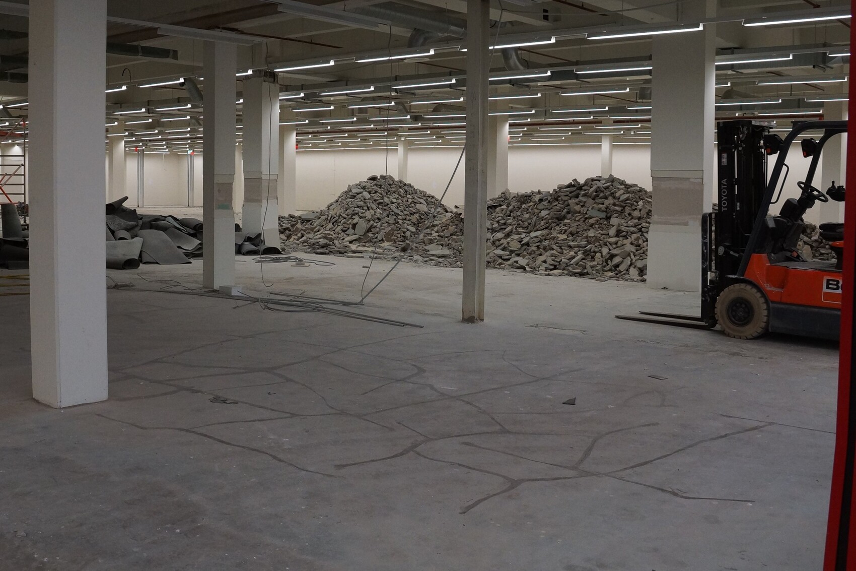 Große Bauhalle mit Säulen, Trümmerhaufen in der Mitte und Gabelstapler rechts.