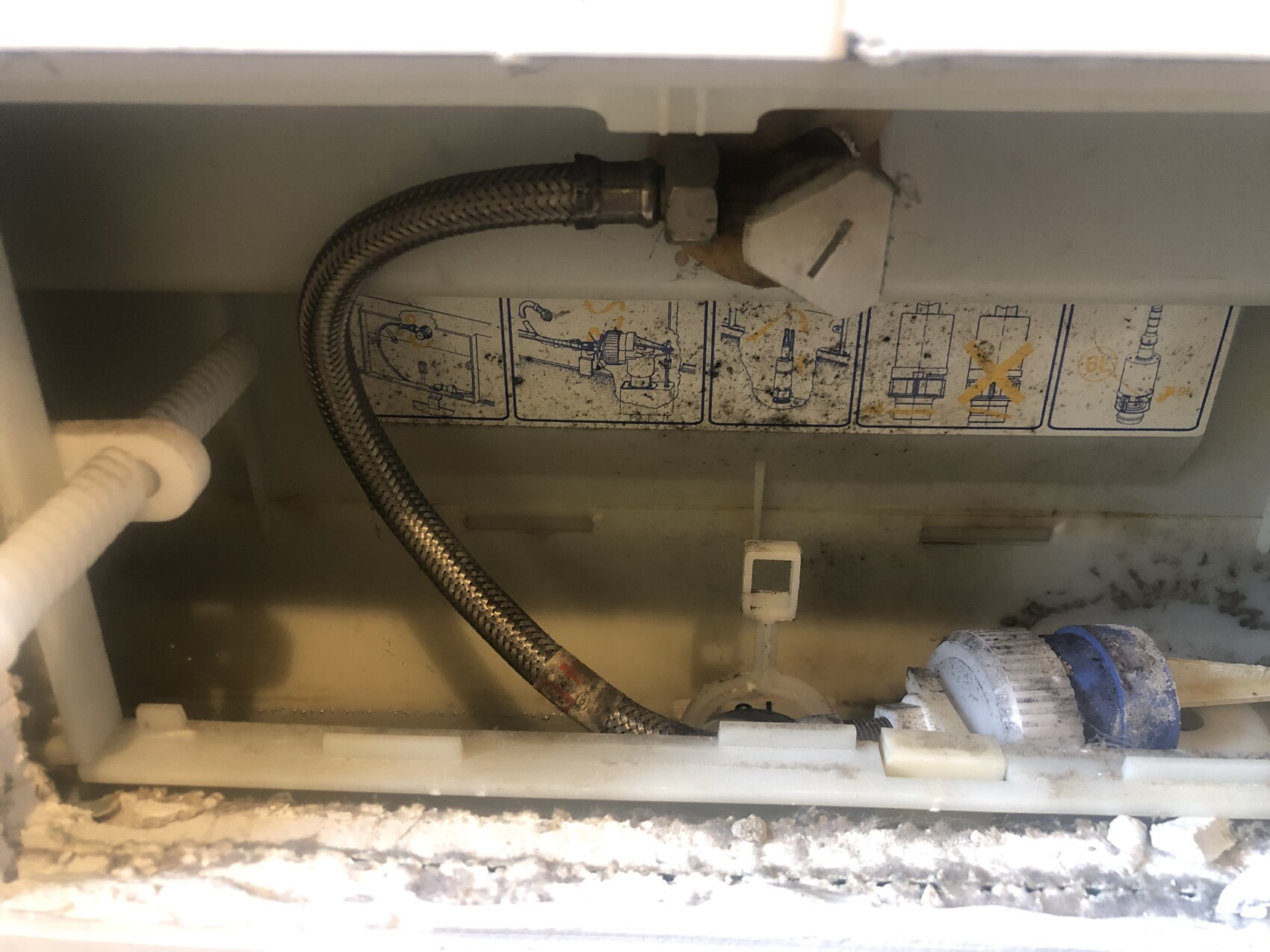 Innenraum eines Geräts mit Edelstahl-Metallflexschlauch, Wasseranschluss und Diagrammaufkleber.