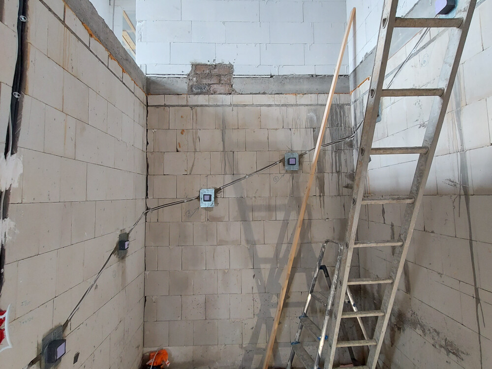Baustelle: geflieste Wände, sichtbare Kabel, Steckdosenboxen und eine Leiter lehnt gegen die Wand.