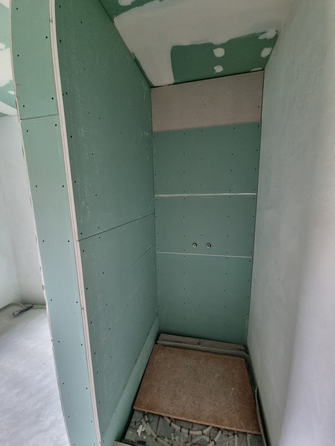 Nische mit grünem Trockenbau, sichtbare Schraubenlöcher, Bodenplatte und Baumaterialreste.