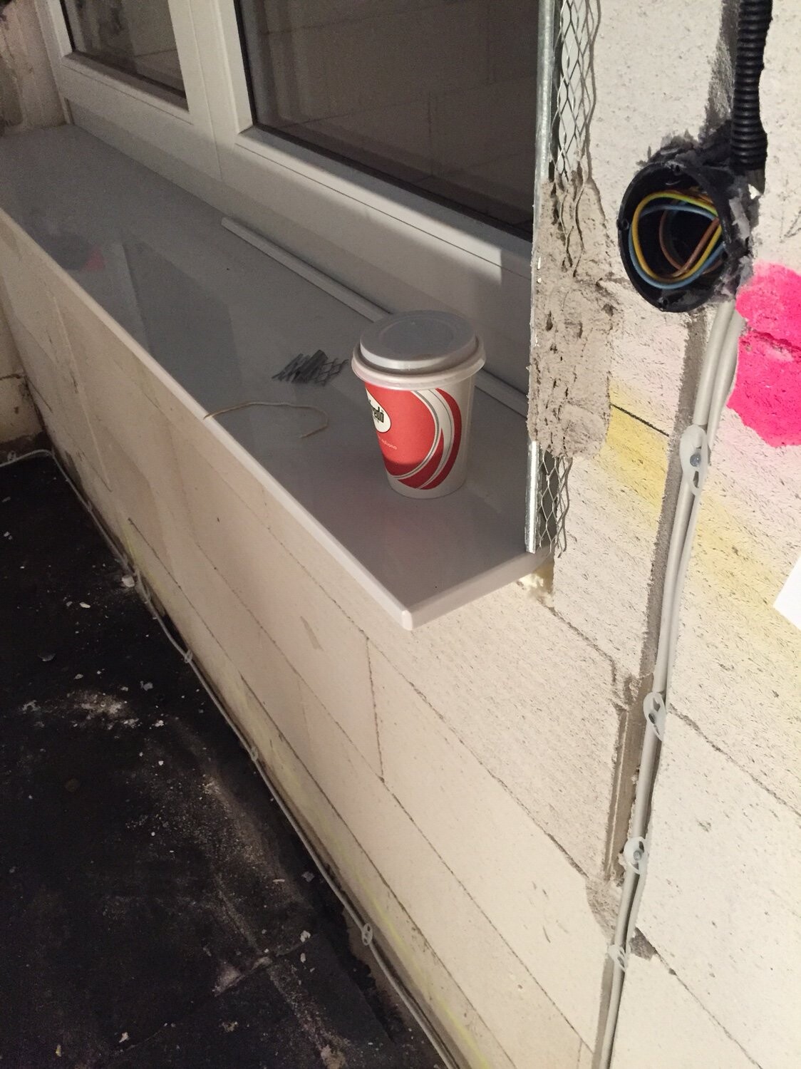 Kaffeebecher auf provisorischer Fensterbank; offenliegender Kabelkanal in Wand.