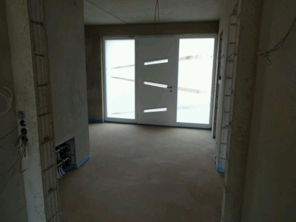 Unfertiger Innenraum einer Baustelle mit Glastür und sichtbarer Elektroinstallation
