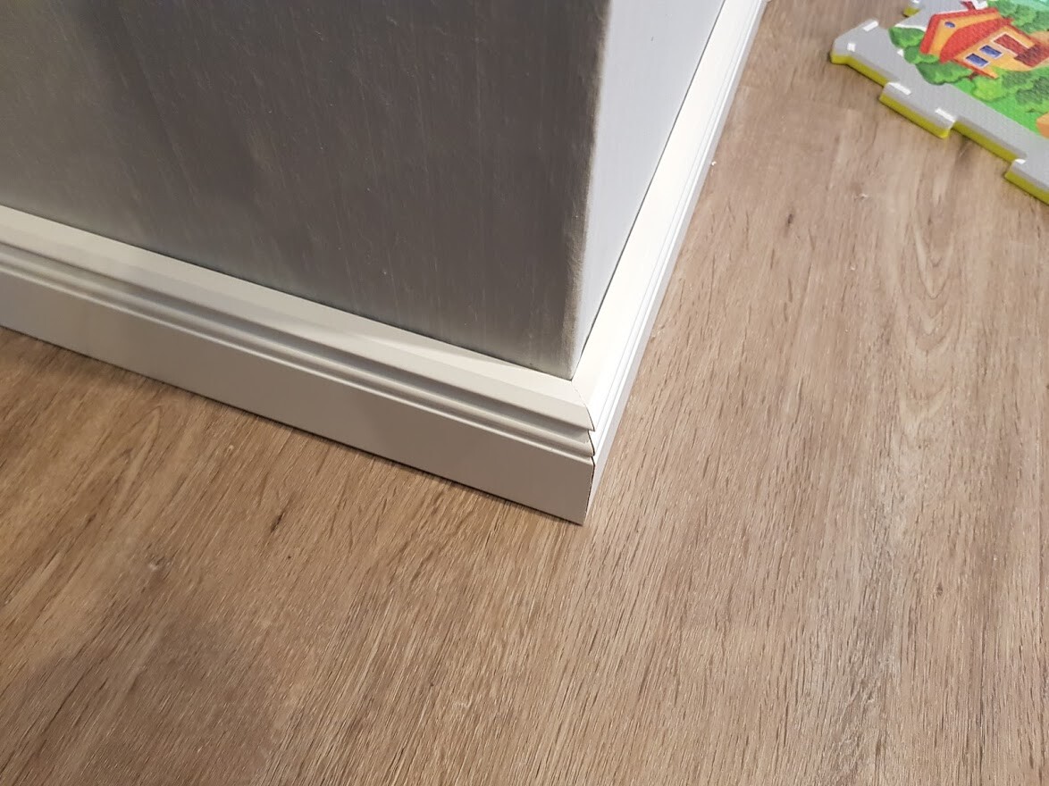 Unterer Bereich einer Edelstahl-Tür mit Weißrahmen auf Holzboden, Spielzeug im Hintergrund.