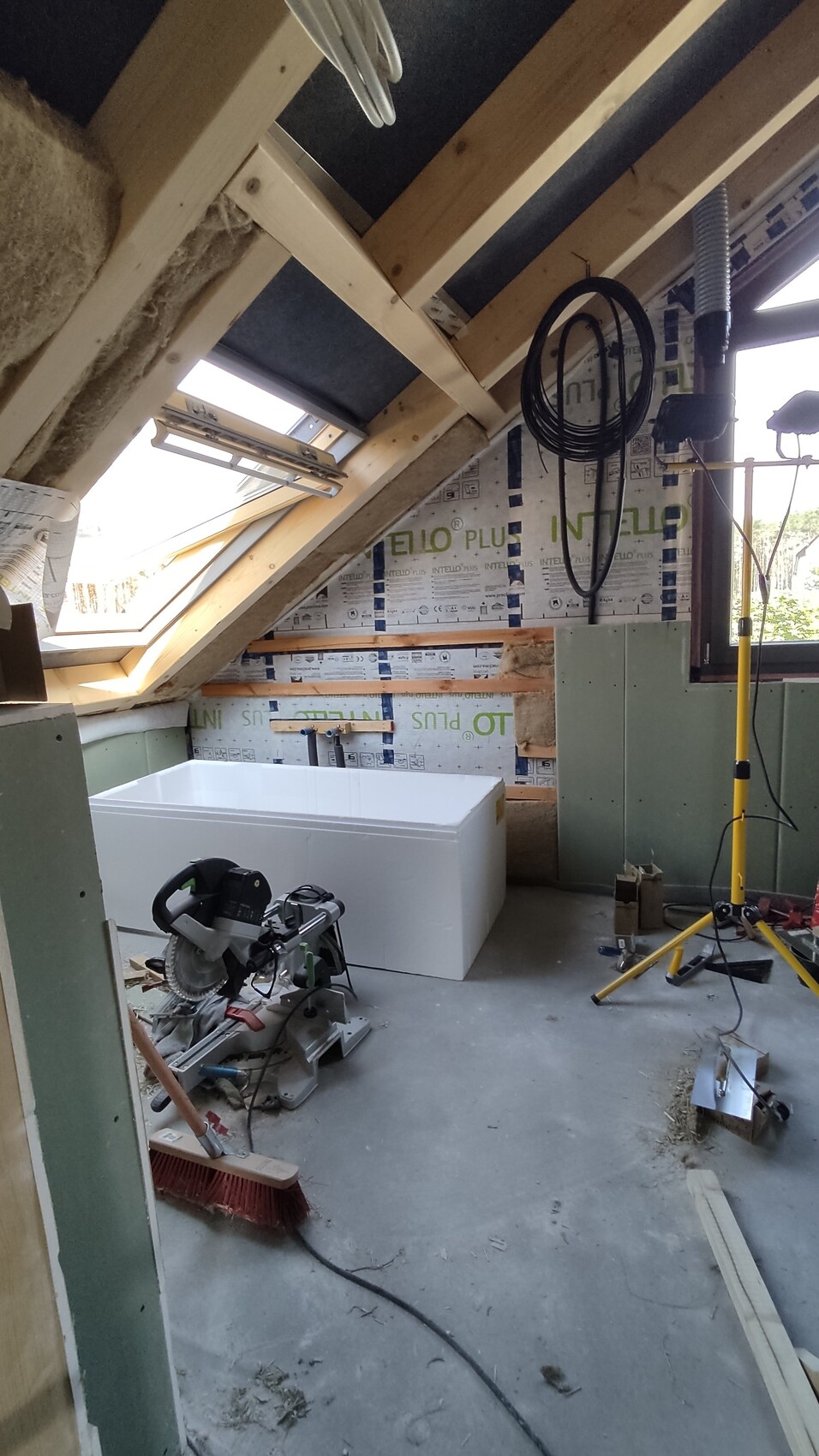 Rohbau-Dachgeschoss mit freistehender Badewanne, Werkzeugen, Kabeln und Baumaterialien.