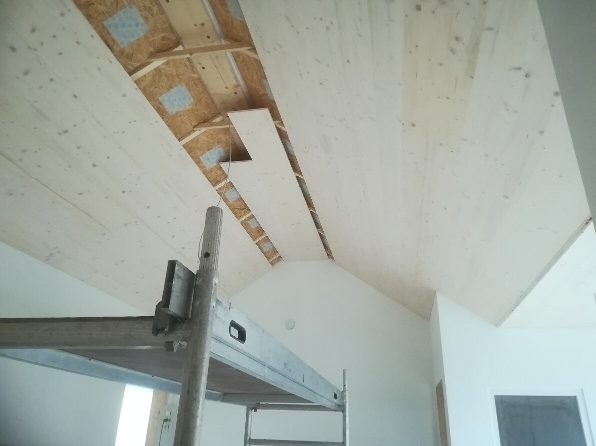 Unbearbeiteter Innenraum mit OSB-Decke, Baugerüst und weißen Wänden.