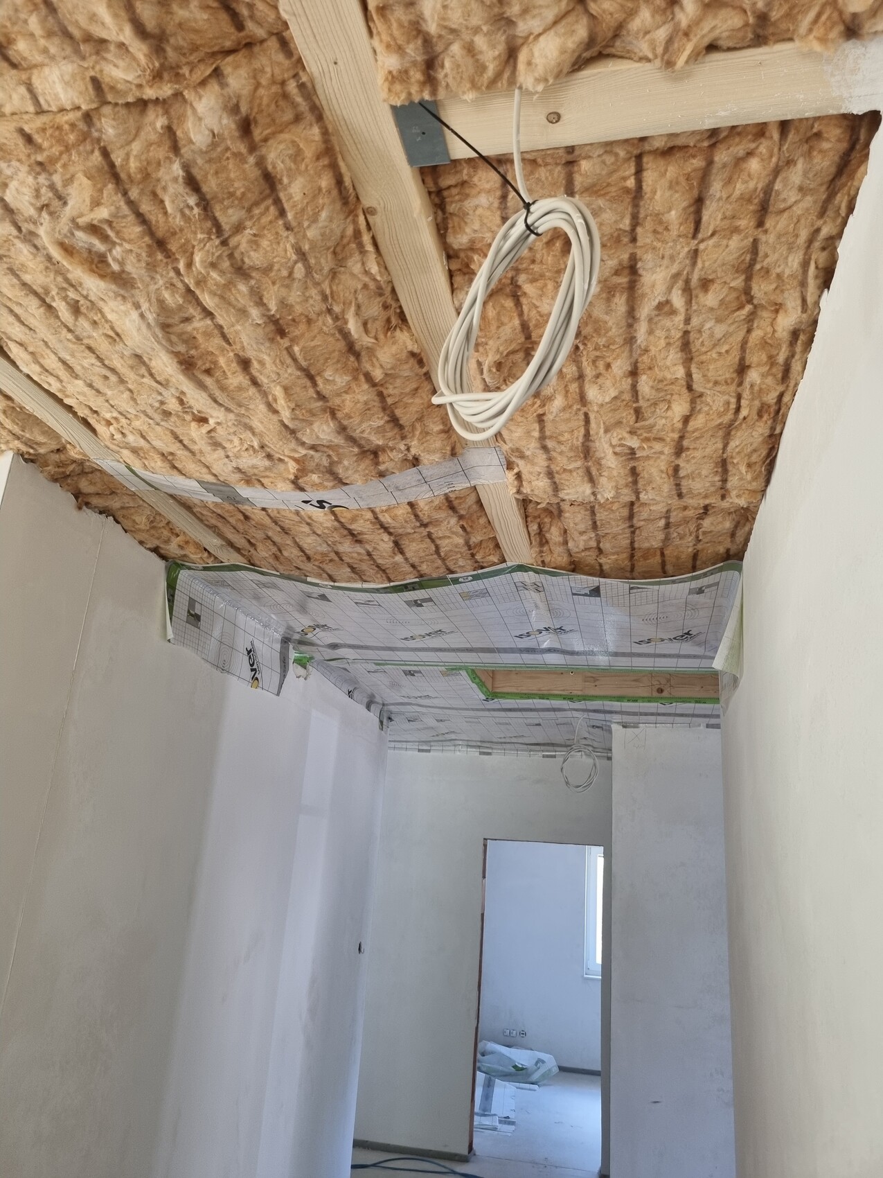 Baustelle: Decke mit Mineralwolle-Dämmung, Holzlatten, Kabelbündel, Durchgang zu anderem Raum.