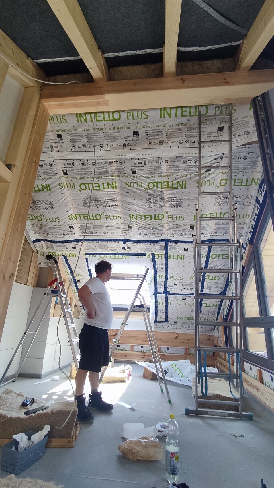 Mann im Bauzimmer mit Leiter, INTELLO PLUS-Dämmung an Wänden, Baustellenmaterialien