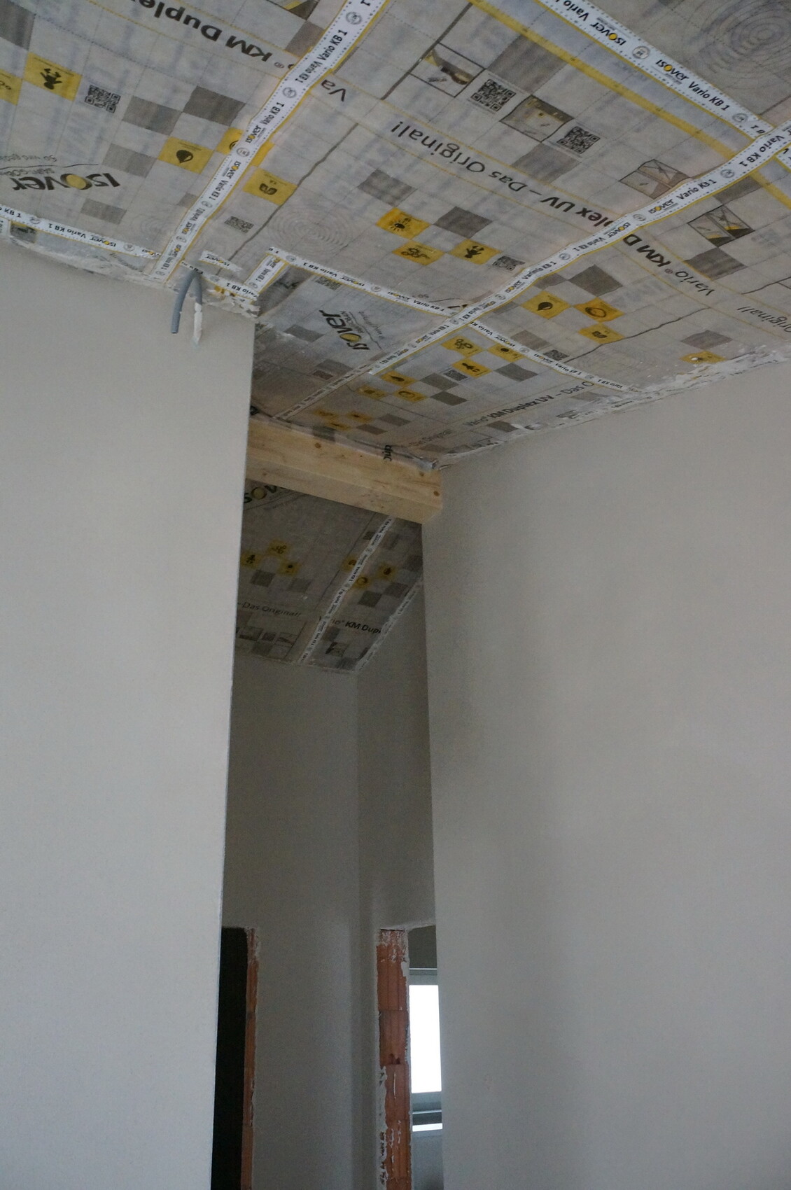 Innenraum mit Decke aus Zeitungspapier, Holzbalken und offener Türöffnung.