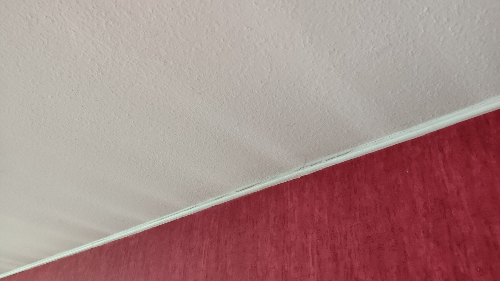 Beige Decke mit Struktur trifft rote Wand, Weisse Zierleiste an der Kante.