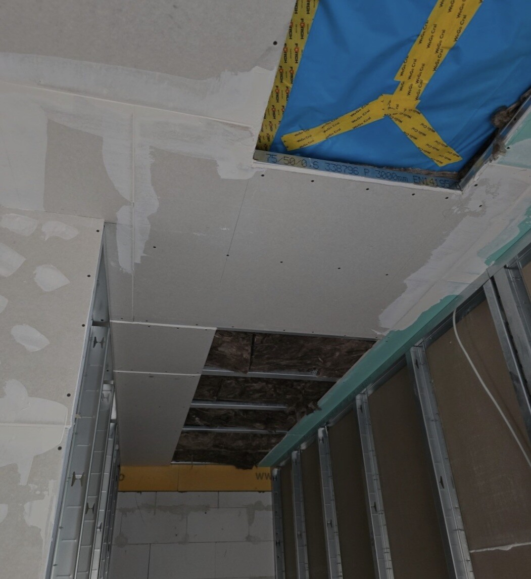 Baubaustelle: Decke aus Trockenbauplatten an Metallständern, offenes Loch mit blauer Abdeckung.