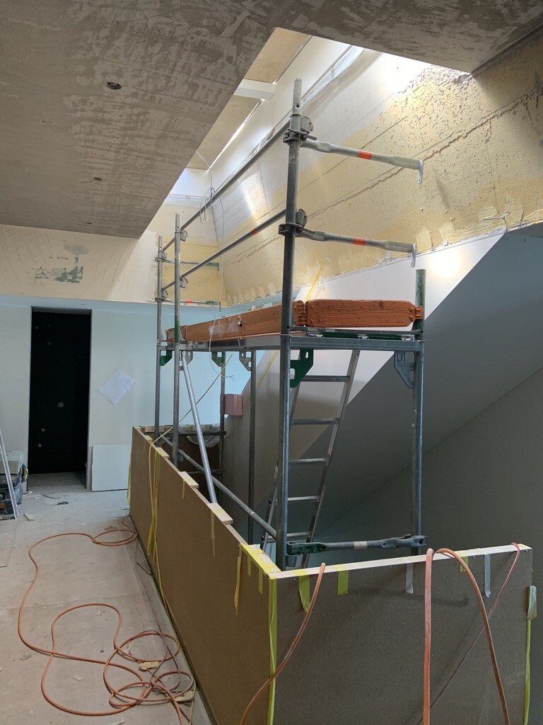 Innenraum einer Baustelle: Gerüst um Treppenöffnung, Bauholz, gelbes Absperrband, Kabel am Boden