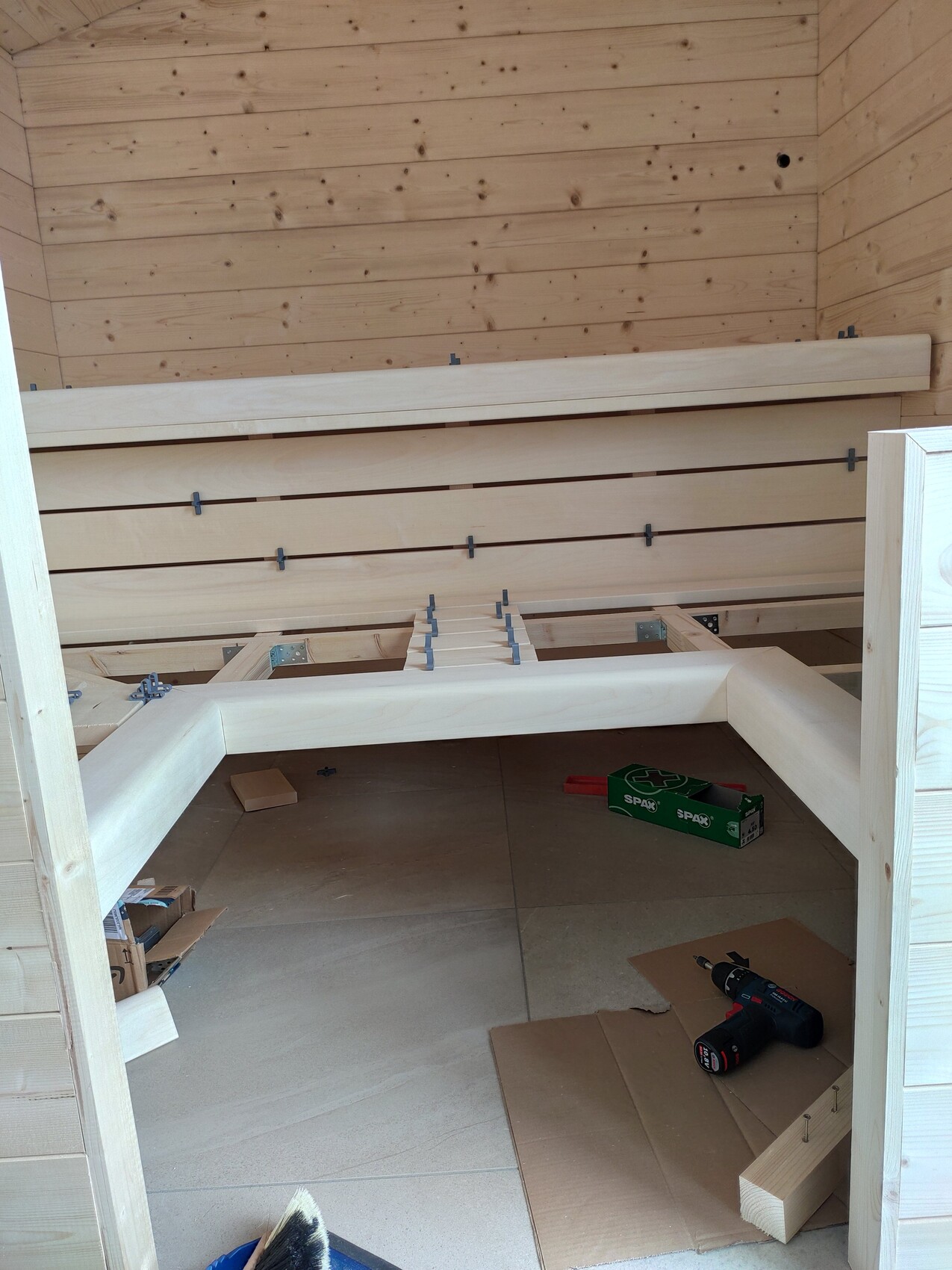 Holzraum mit aufgebauter Bankkonstruktion; Bohrmaschine und Werkzeug auf dem Boden.