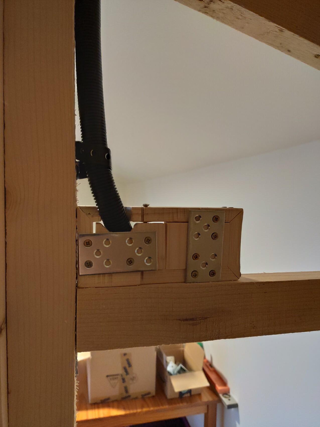Holzrahmen mit Metallwinkelplatten und schwarzem Kabelrohr; Hintergrund Kartons