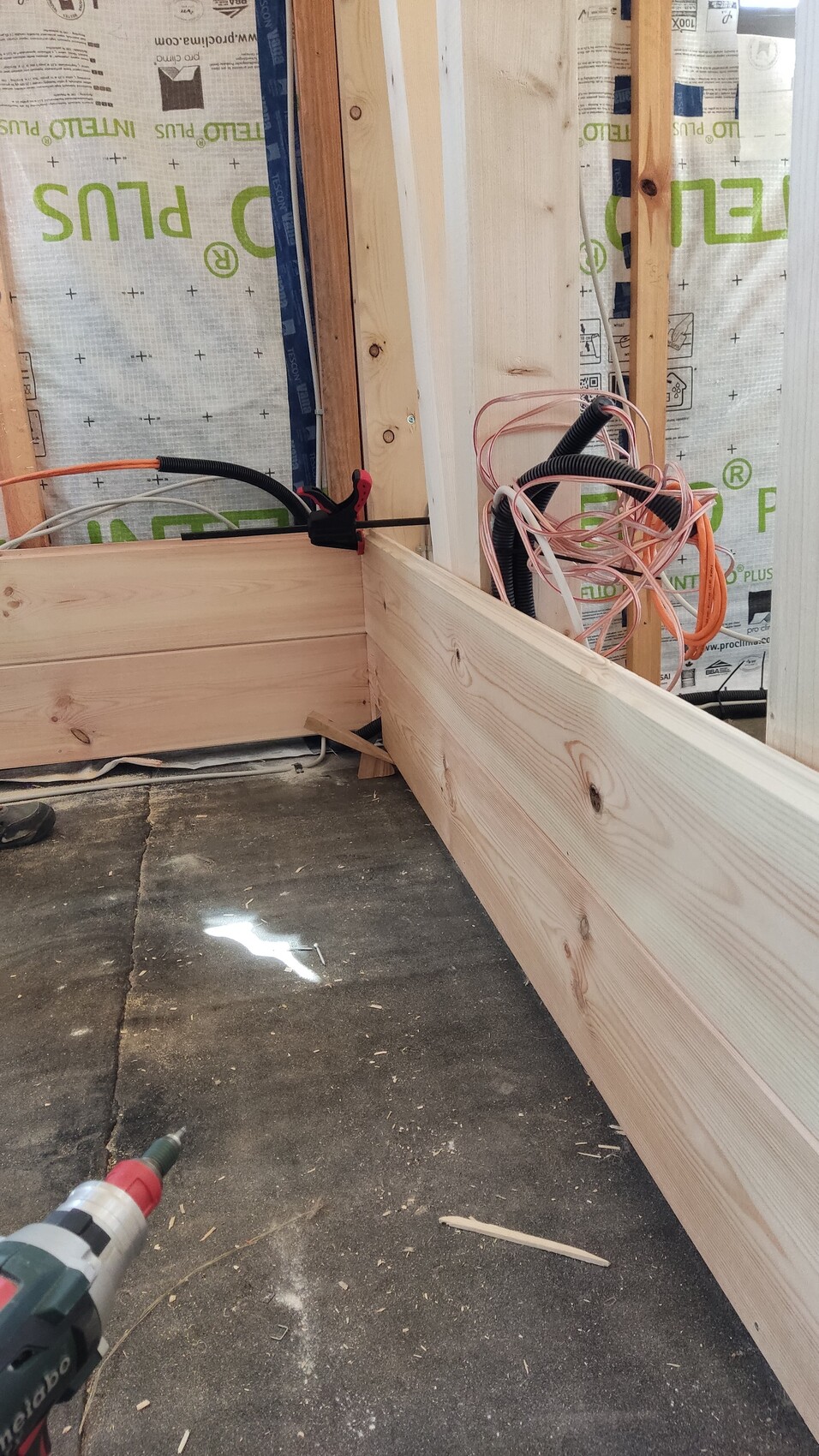Baustelle mit Holzrahmen, Kabelsalat und Bohrer auf staubigem Boden.