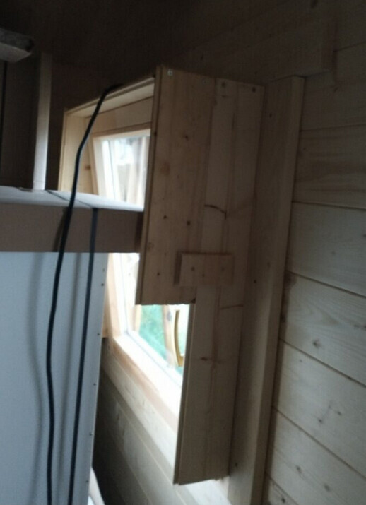 Holzinnenraum: Fenster in Holzwand, sichtbare Holzverkleidung und ein Kabel daneben.