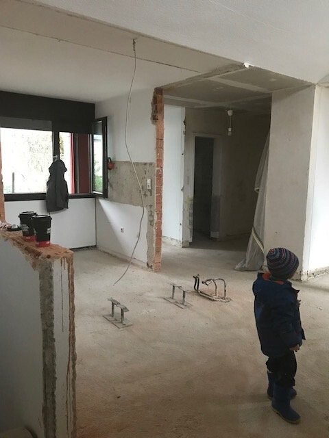 Kind in Winterjacke schaut auf unfertigen Innenraum mit freigelegten Wänden und Bauarbeiten.