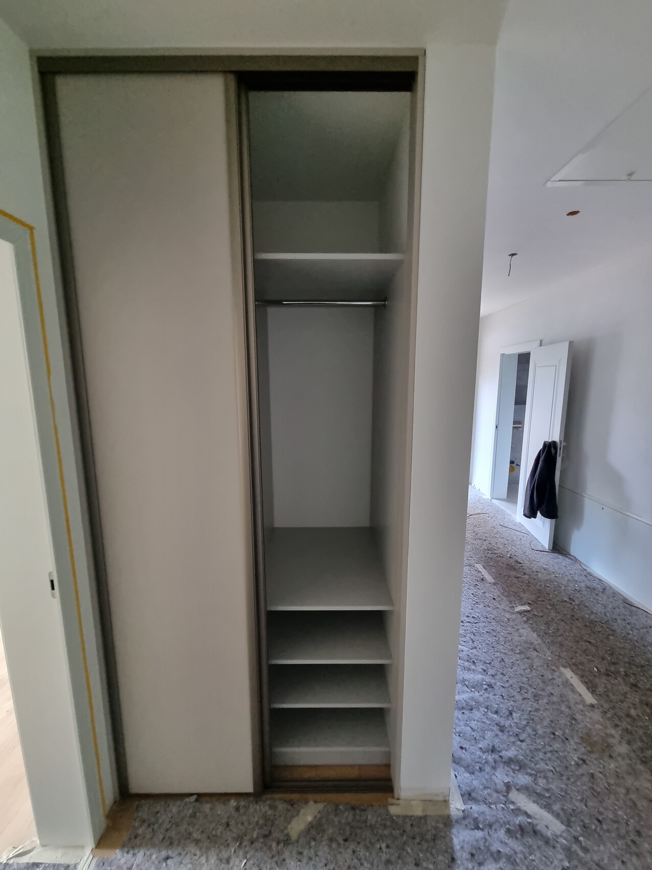 Offener Einbauschrank mit Kleiderstange und Regalböden in einem renovierten Raum.