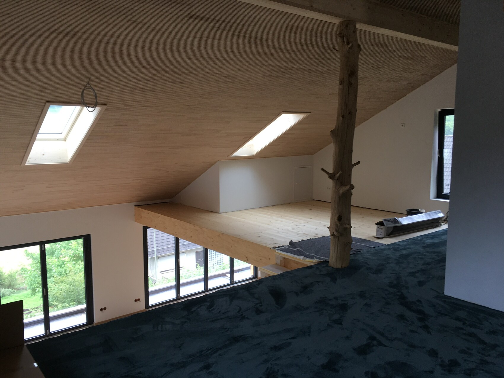 Loftartiges Dachgeschoss im Bau: Holzboden, geneigte Holzdecke, Dachfenster, Baumstamm-Säule.