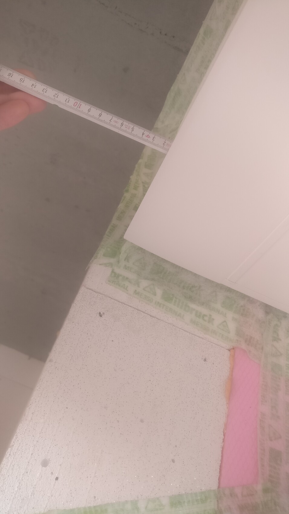 Nahaufnahme eines Maßbands im Innenausbau, grün-weißes Dichtband und pinke Dämmplatte sichtbar