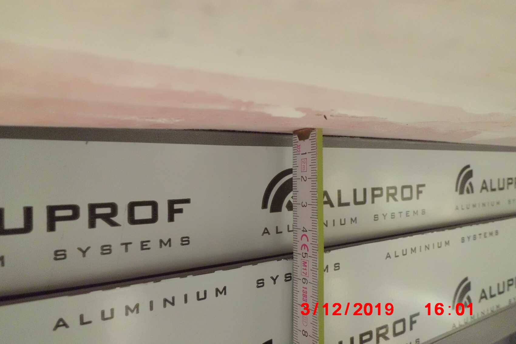 Vertikales Messband an einer Holzplatte, Hintergrund zeigt ALUPROF-Aluminium-Systeme.