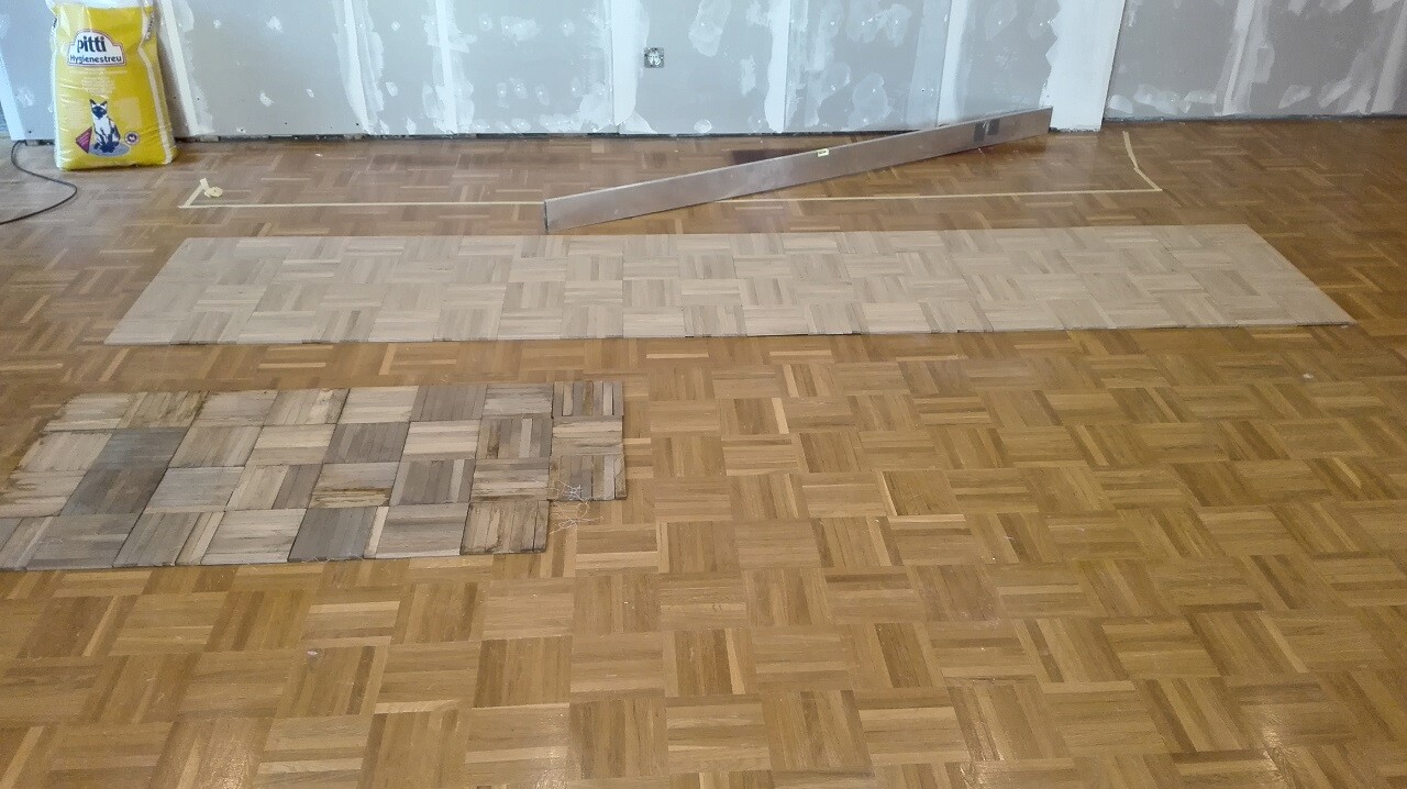 Wohnzimmerboden mit verlegtem Parkett und Baumaterialien im Hintergrund.