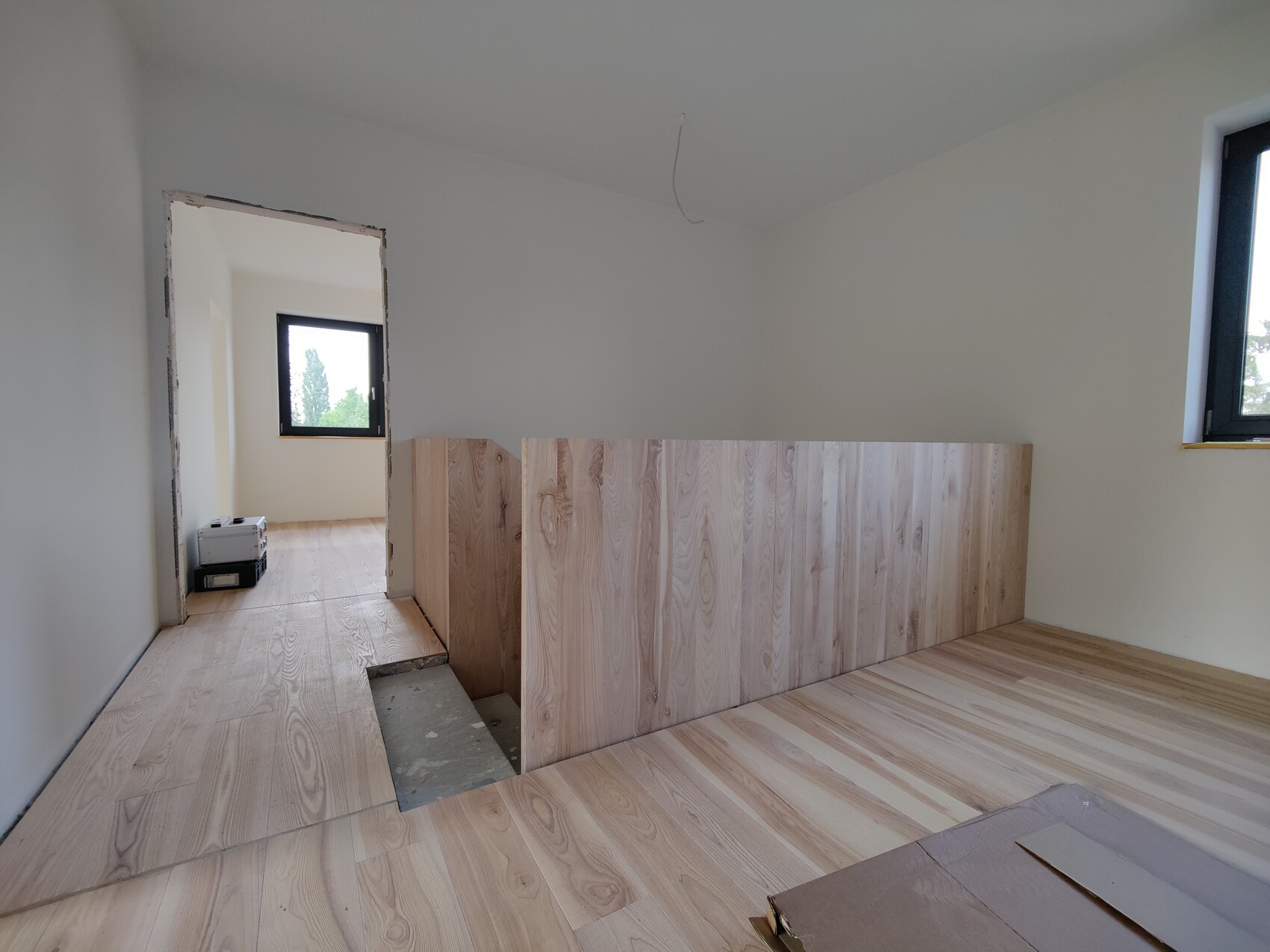 Baustellenraum mit Holzboden, provisorischer Holzwandverkleidung, Fenster, Werkzeugkiste.