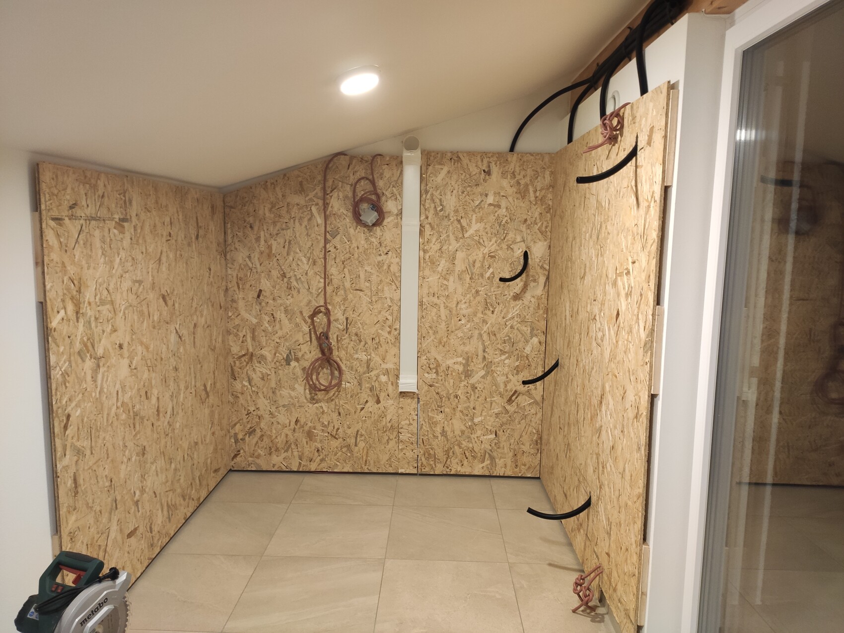 Rohbauzimmer mit OSB-Wänden, hängenden Kabeln und Säge auf dem Boden