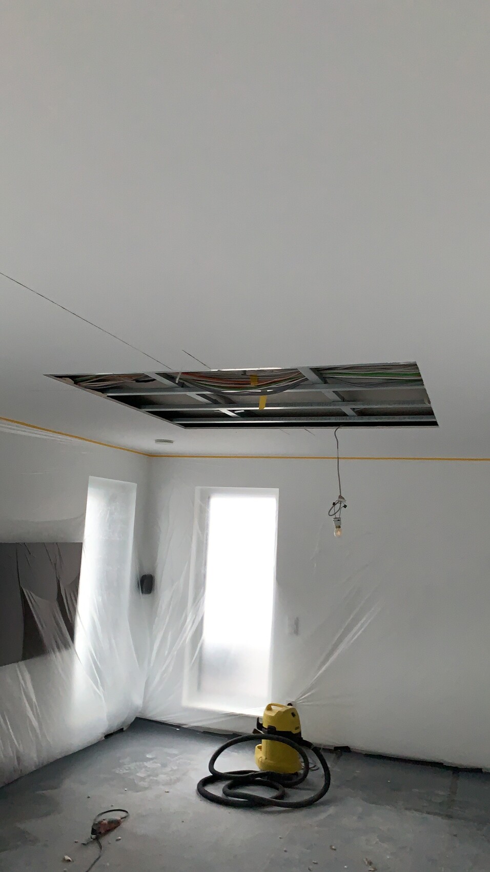 Rohbauzimmer mit offener Decke, Kabeln, Hängelampe, Plastikfolie und Staubsauger.