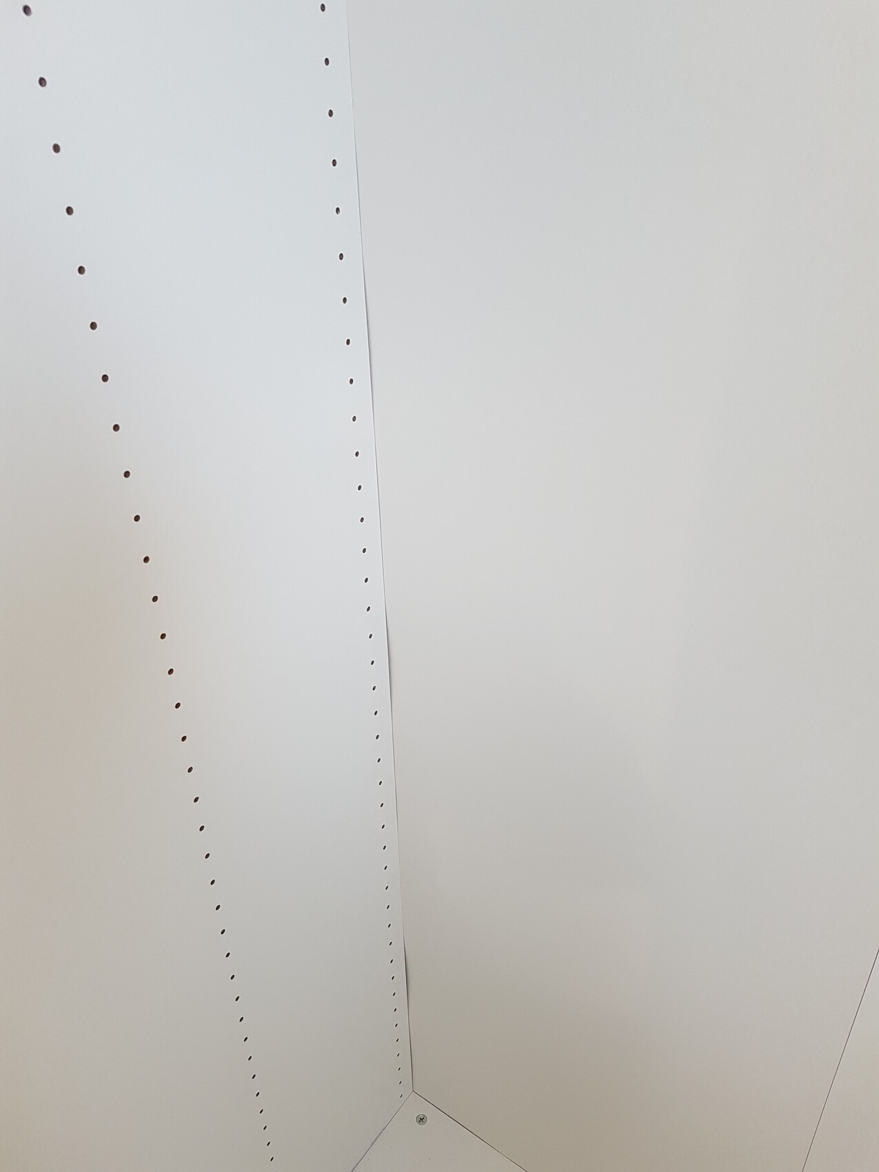 Weißes Innenwandpaneel mit vielen Bohrlöchern in einer Ecke