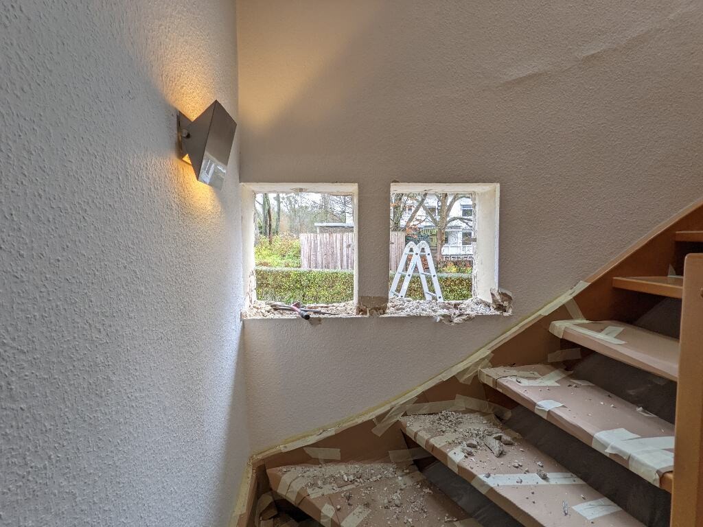 Renoviertes Treppenhaus mit Staub, zwei Fensteröffnungen, Außenleiter sichtbar