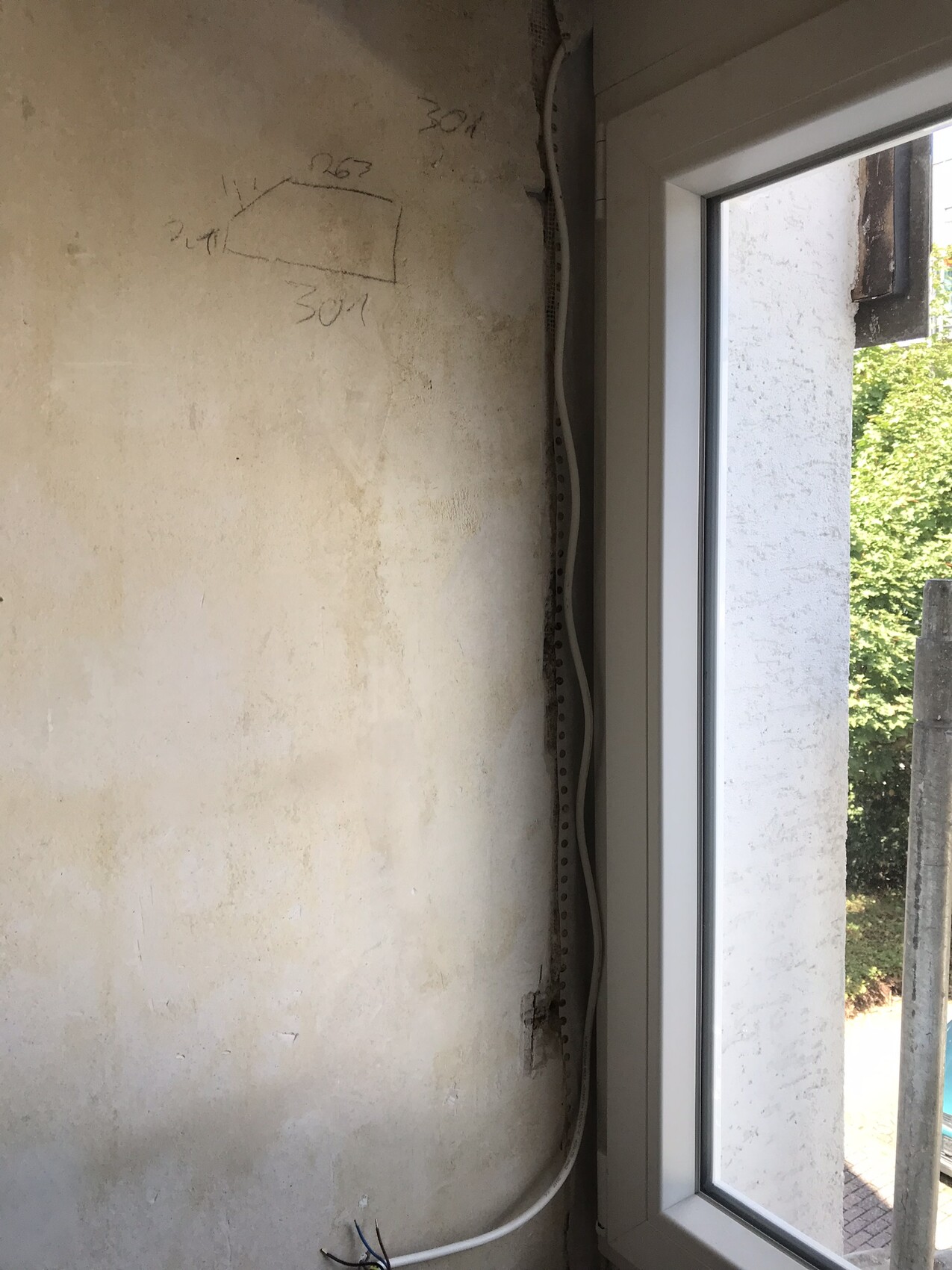 Rohverputzte Wand mit Skizze, Kabelkanal und Fensterblick nach draußen.