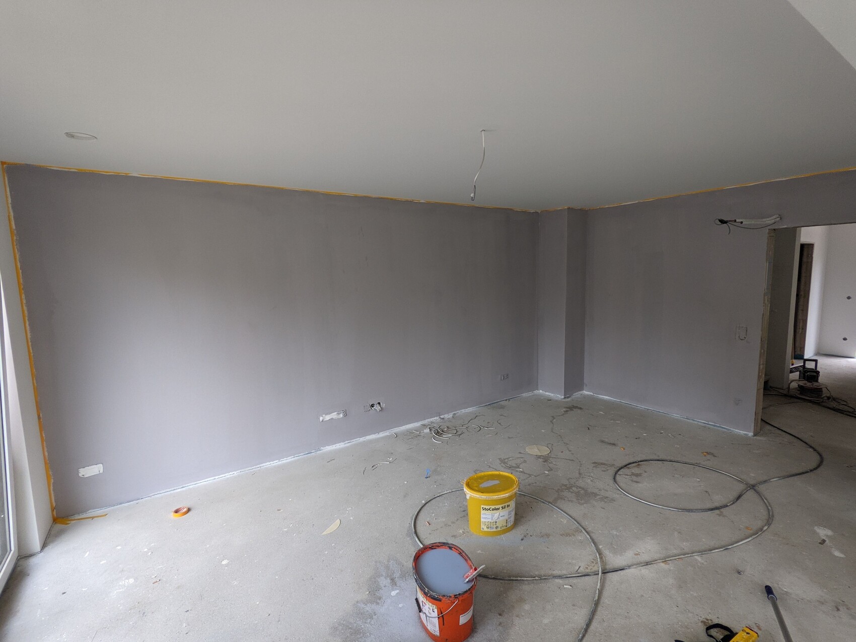 Renovierungsraum mit grauen Wänden, lose Kabel, Farbdosen und Baumaterial auf dem Betonboden.