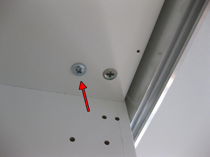 Weißes Möbelbauteil mit zwei Schrauben, Metallrahmen und Bohrlöchern.
