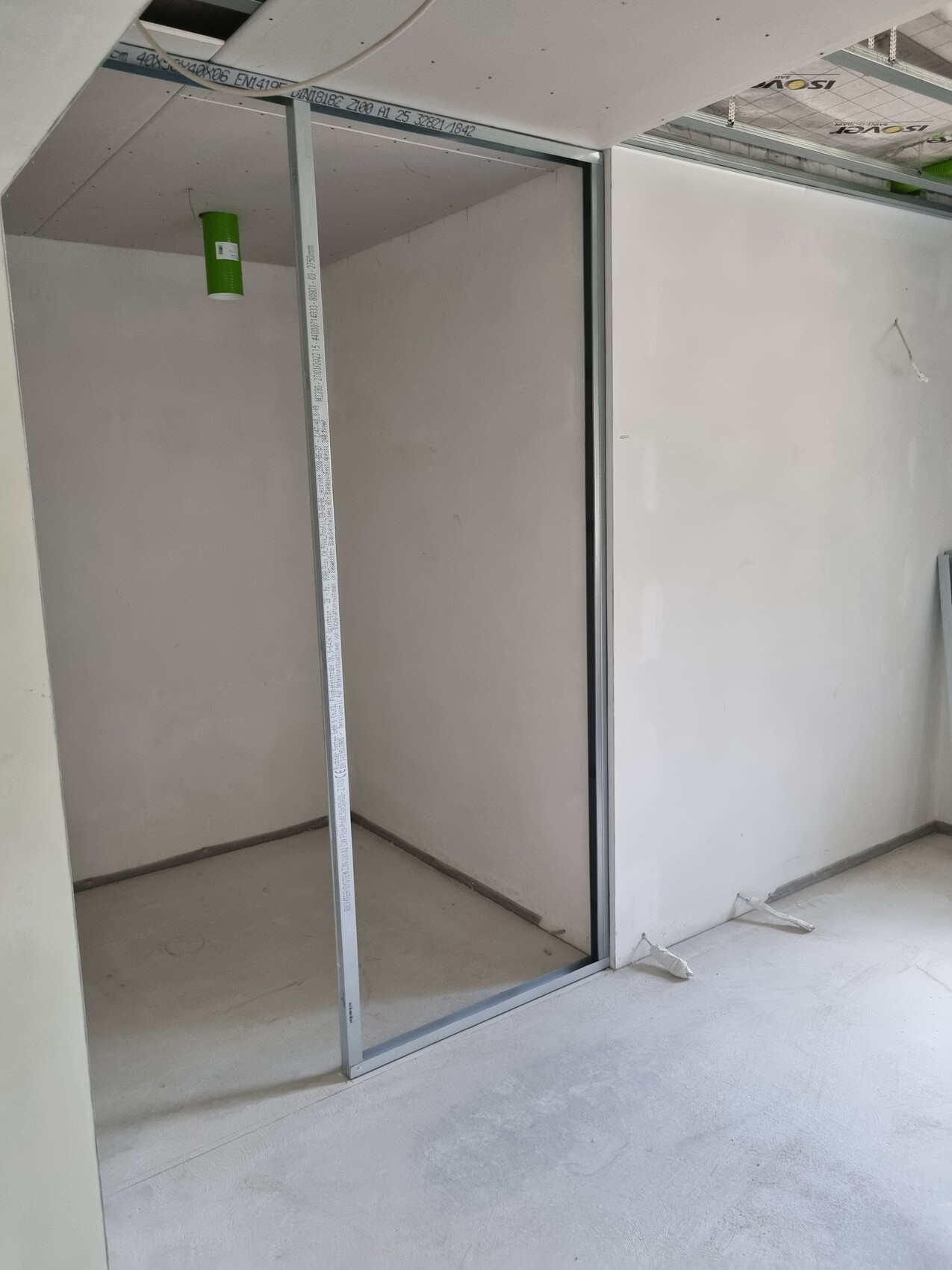Unfertiger Innenraum mit Metallständerwand, offener Tür; Messlatte in der Nische.