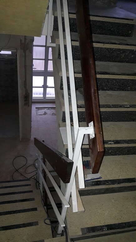 Innenansicht einer Treppe mit weißem Geländer und dunklen Stufen während Bauarbeiten.