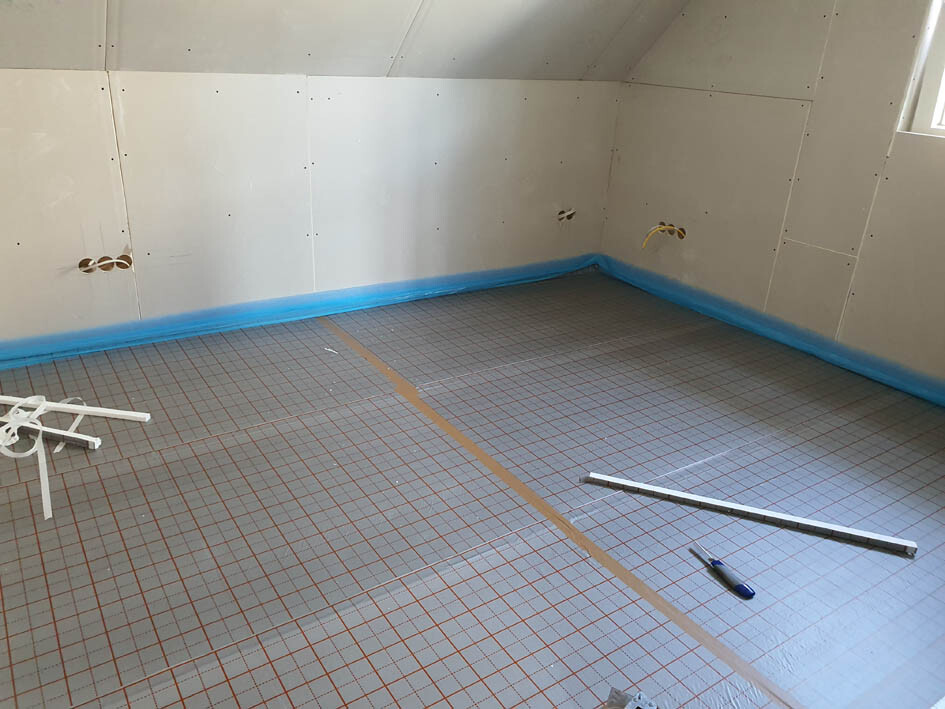 Bauzimmer mit Trockenbauwänden, blauer Randabdichtung am Boden, Rohinstallationen.