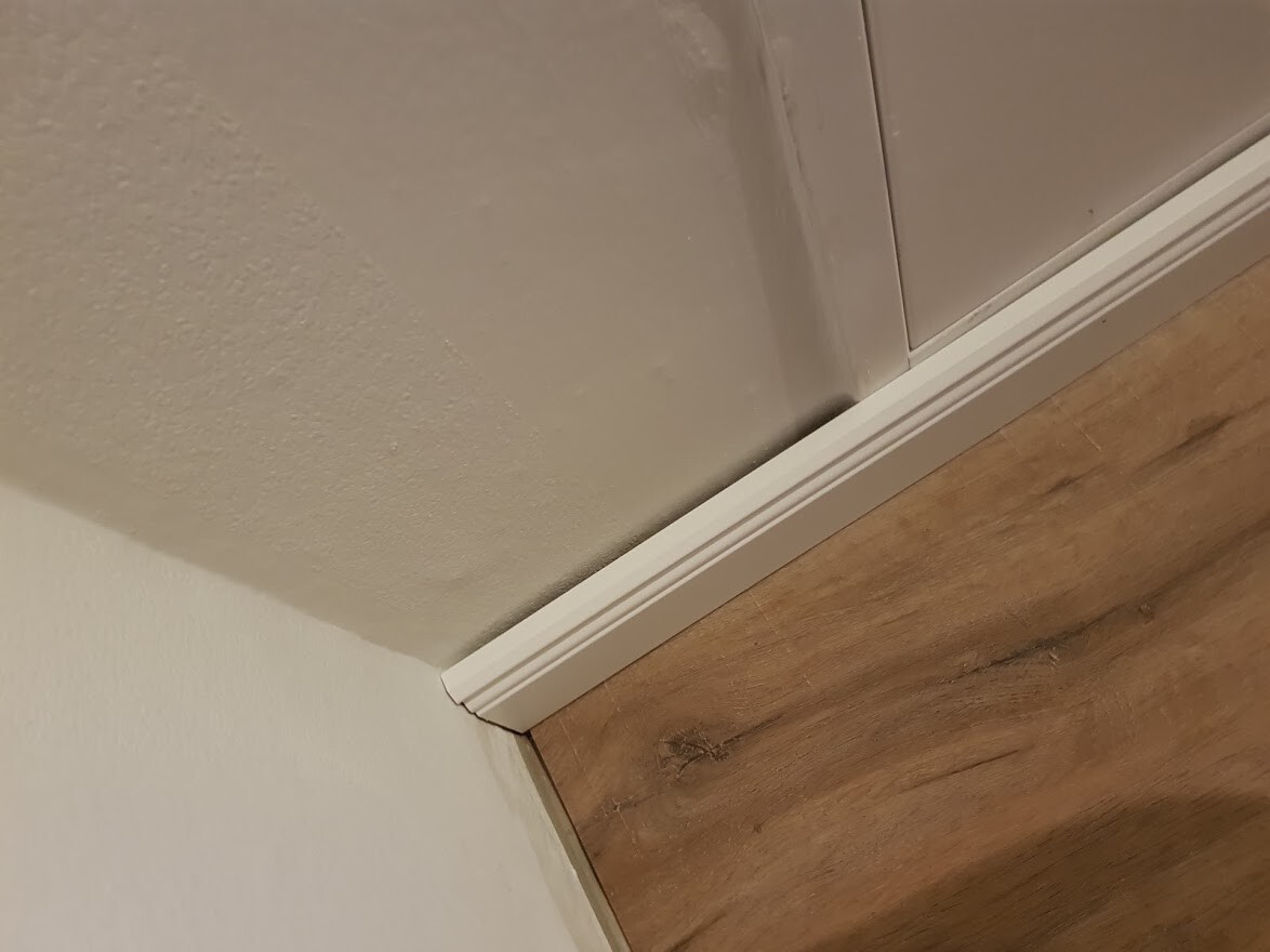 Weiße Fußleiste in einer Innenecke neben Holzboden und Schrankfront.