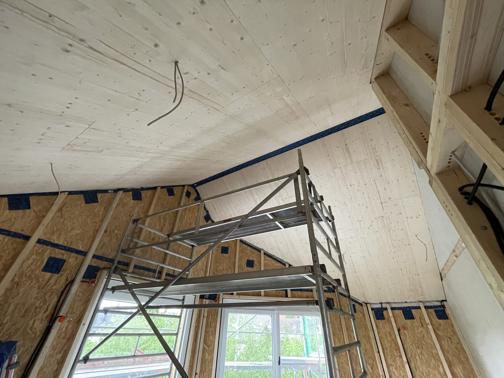 Dachboden-Bau: Metallgerüst vor OSB-Wänden, unbehandeltes Holz, Kabel von der Decke, Fenster unten.