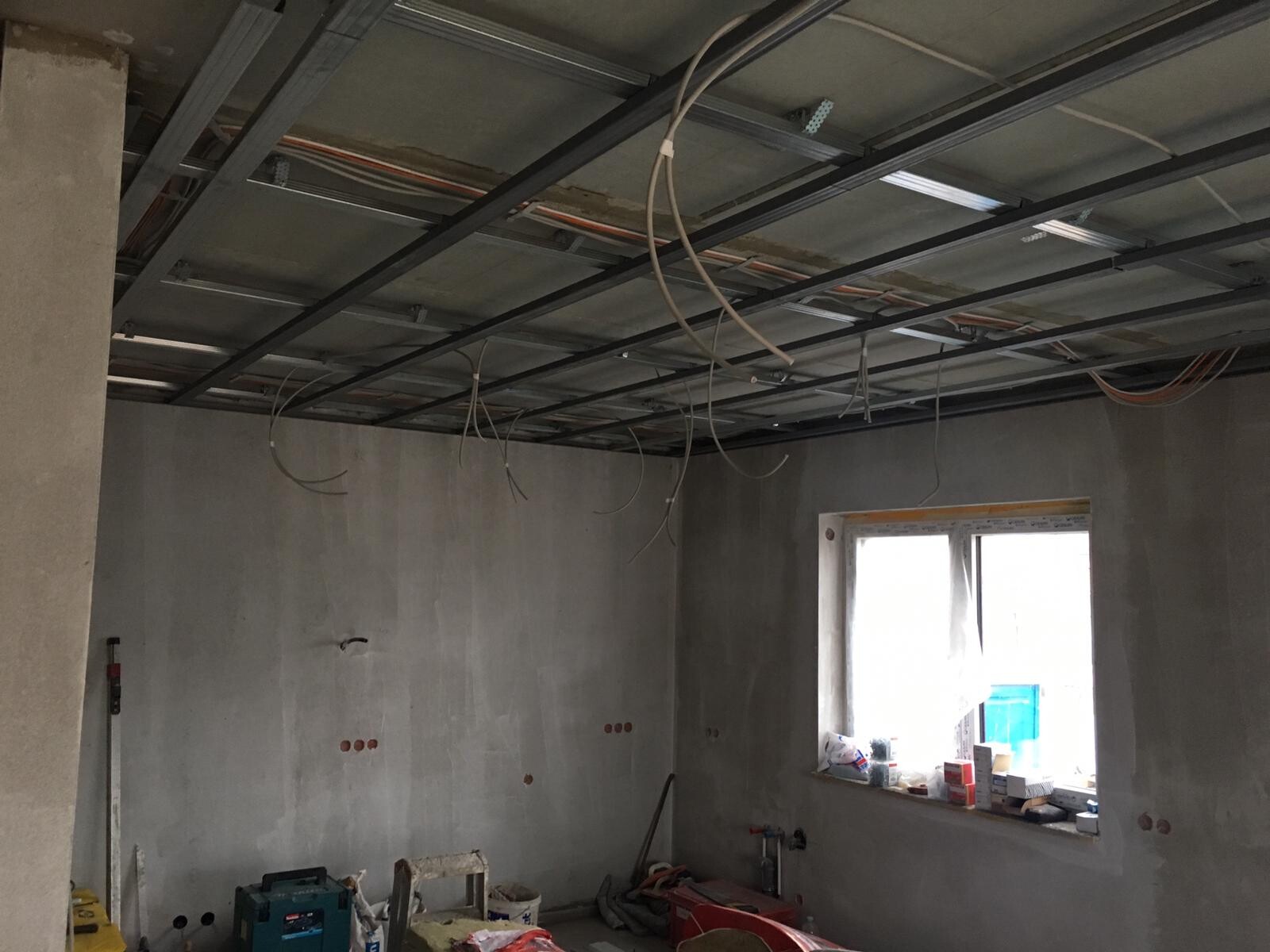Renovierungsraum mit offener Decke, Stahlträgern, lose Kabeln, unfertigen Wänden und Fenster.