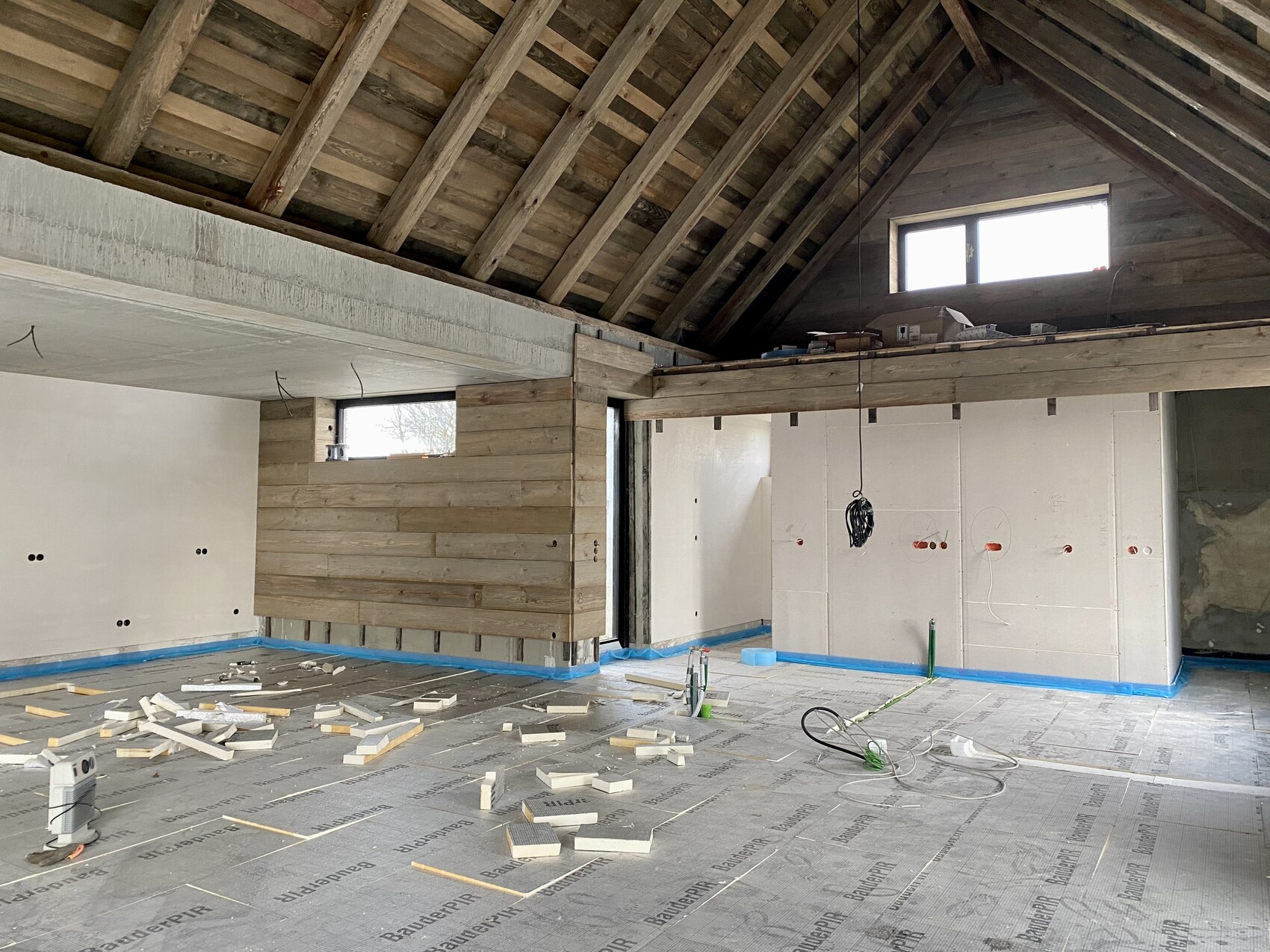 Baustelle im Dachgeschoss: Holzbalkendecke, provisorische Wand, herumliegende Kabel und Bodenfolie.
