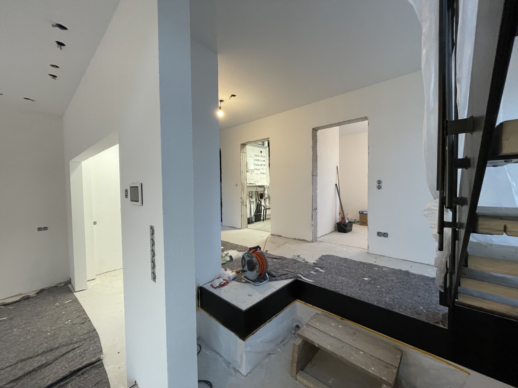 Innenraum einer Renovierungsbaustelle: weiße Wände, rechte Treppe, Werkzeuge am Boden.