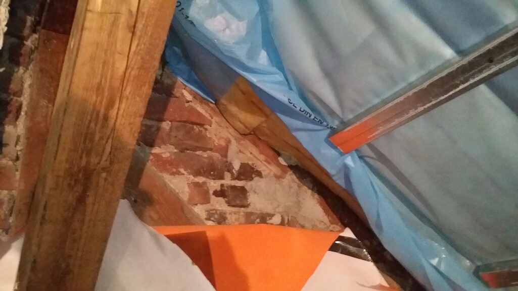 Baustelle mit Ziegelwand, Holzbalken und blauer Abdeckfolie beim Innenausbau.