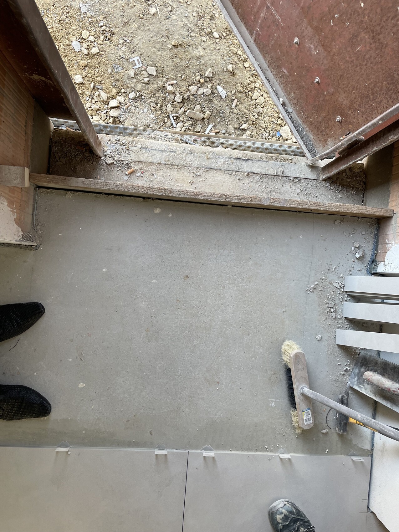 Baustelle im Innenbereich: Betonboden, Reinigungsbesen und Baumaterial.
